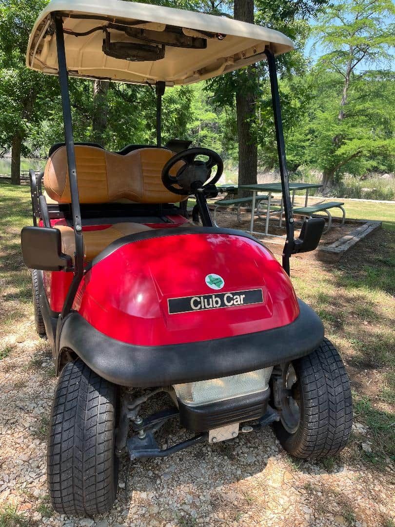 Un carrito de golf rojo con toldo, estacionado en un camino de grava en un parque.