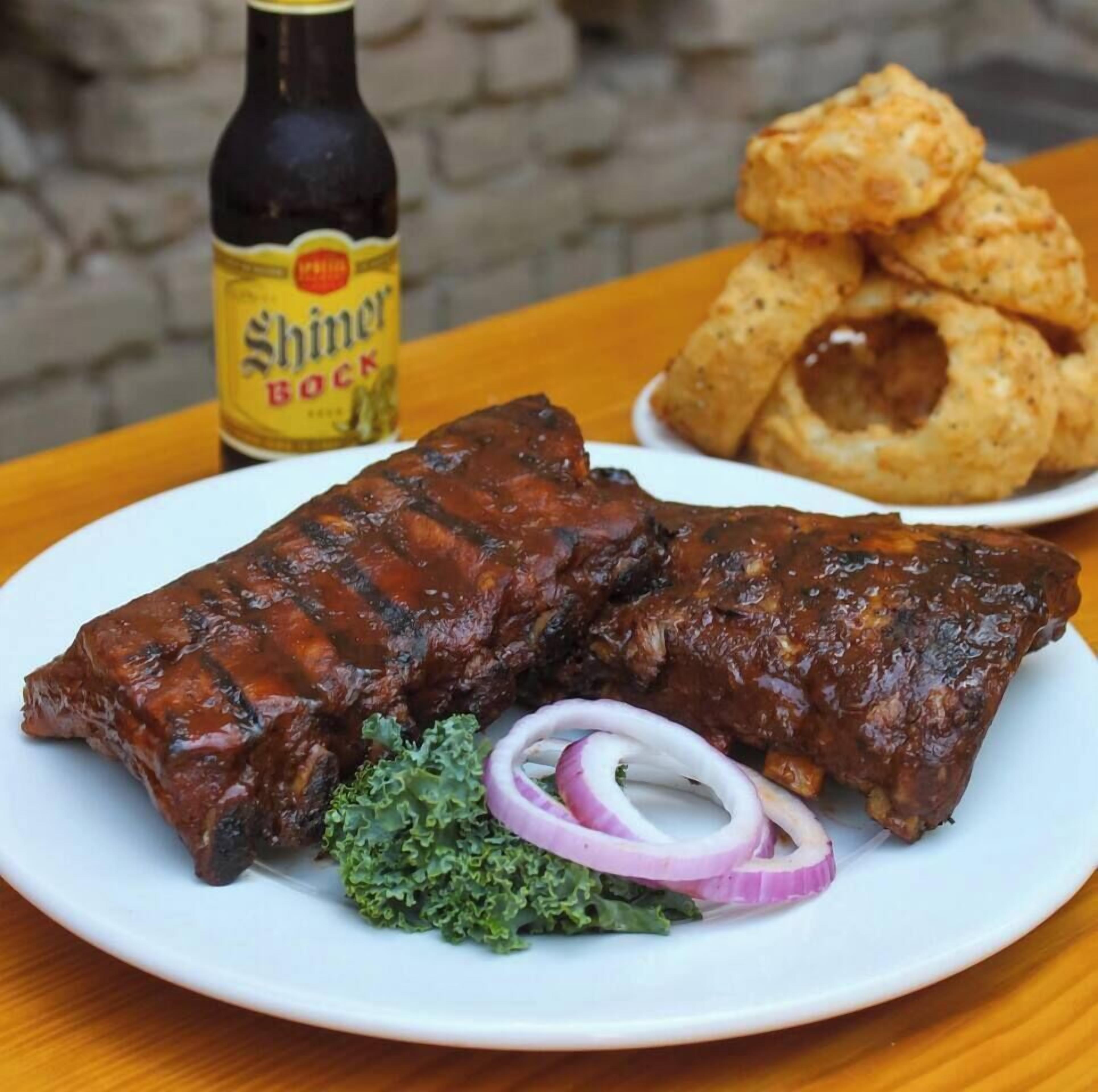A plate with ribs, a bottle of Shiner Bock beer, and fried plantains.