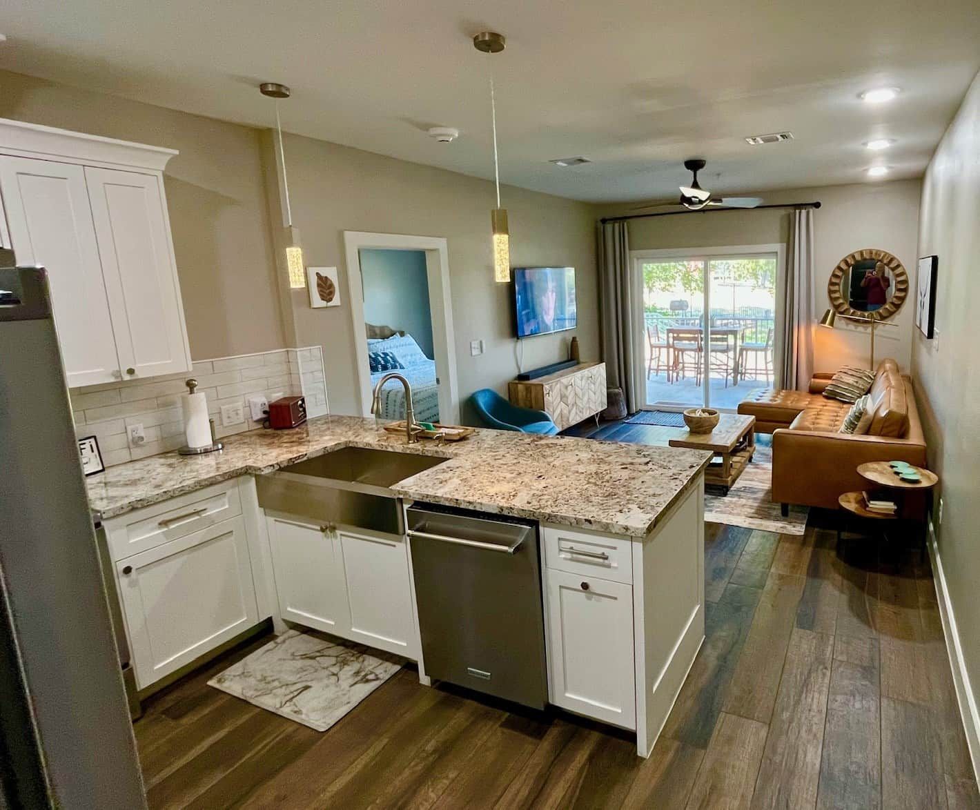 A modern kitchen with white cabinets, a granite countertop, and a dishwasher. There is a dining area with a blue chair and a sofa.
