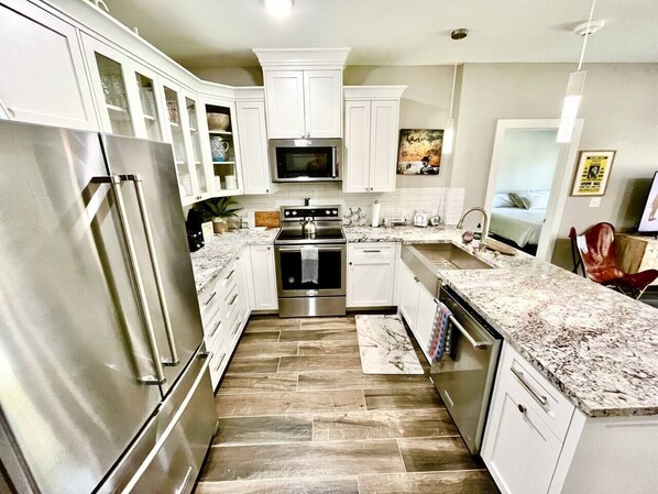 A modern kitchen with white cabinets, stainless steel appliances, and a marble countertop.