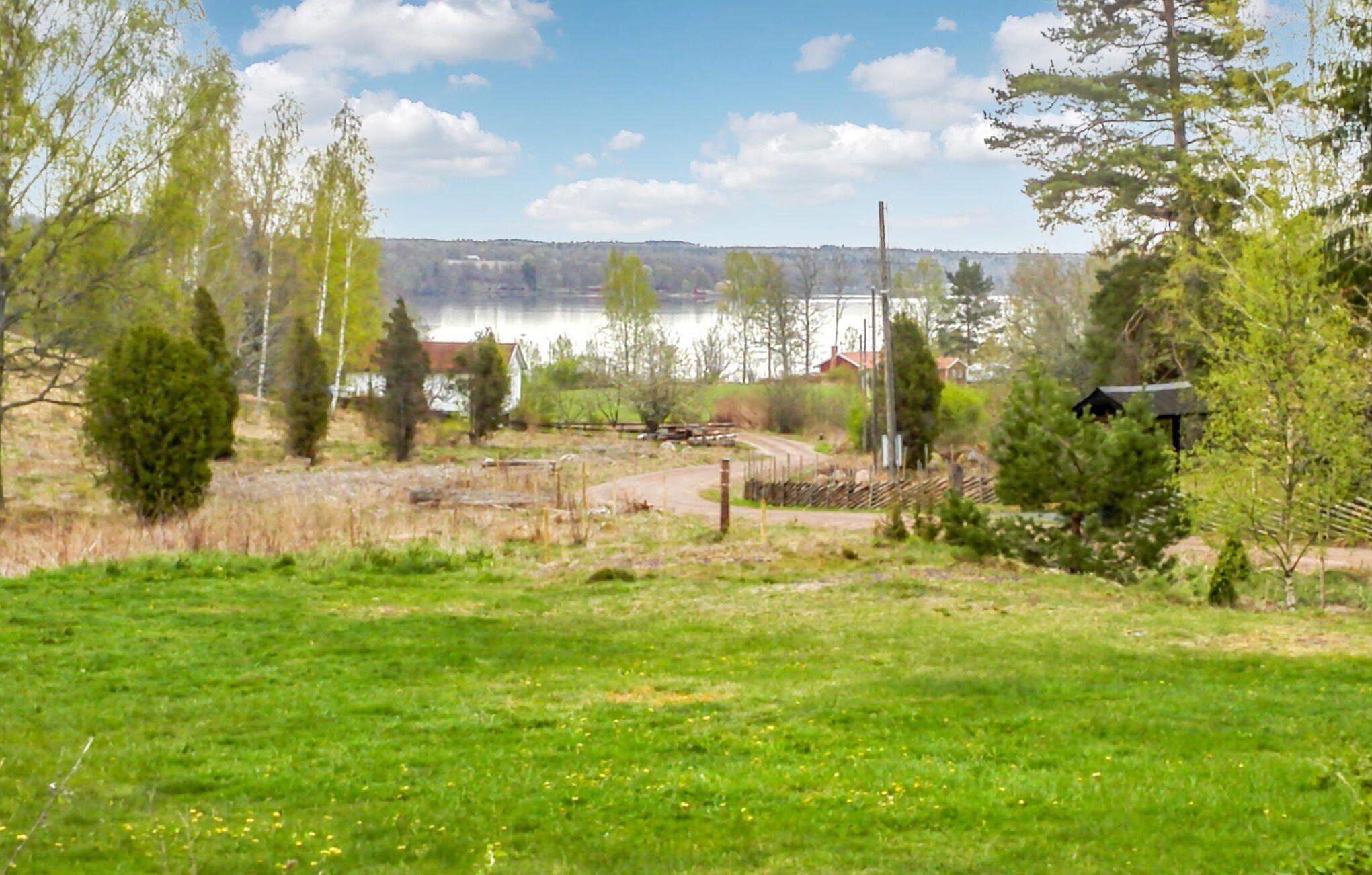A rural landscape with a grassy field, trees, a small building, and a body of water in the background.