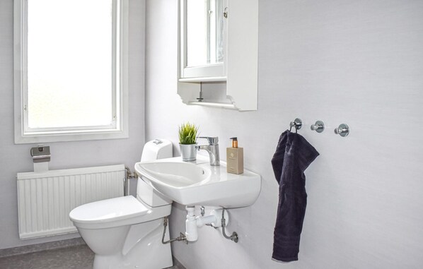 A bathroom with a toilet, sink, and mirror. There is a window, a towel rack, and a radiator. - Lovely home in Tranås with lake view (Tranås)