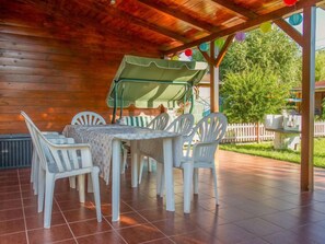 Una terrazza esterna con una pergola in legno, sedie di plastica bianca e un tavolo con ombrellone verde.