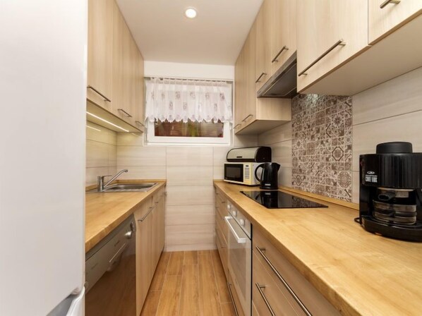 Una cucina compatta con mobili in legno, un forno a microonde, una macchina da caffè e una finestra con tenda decorata.