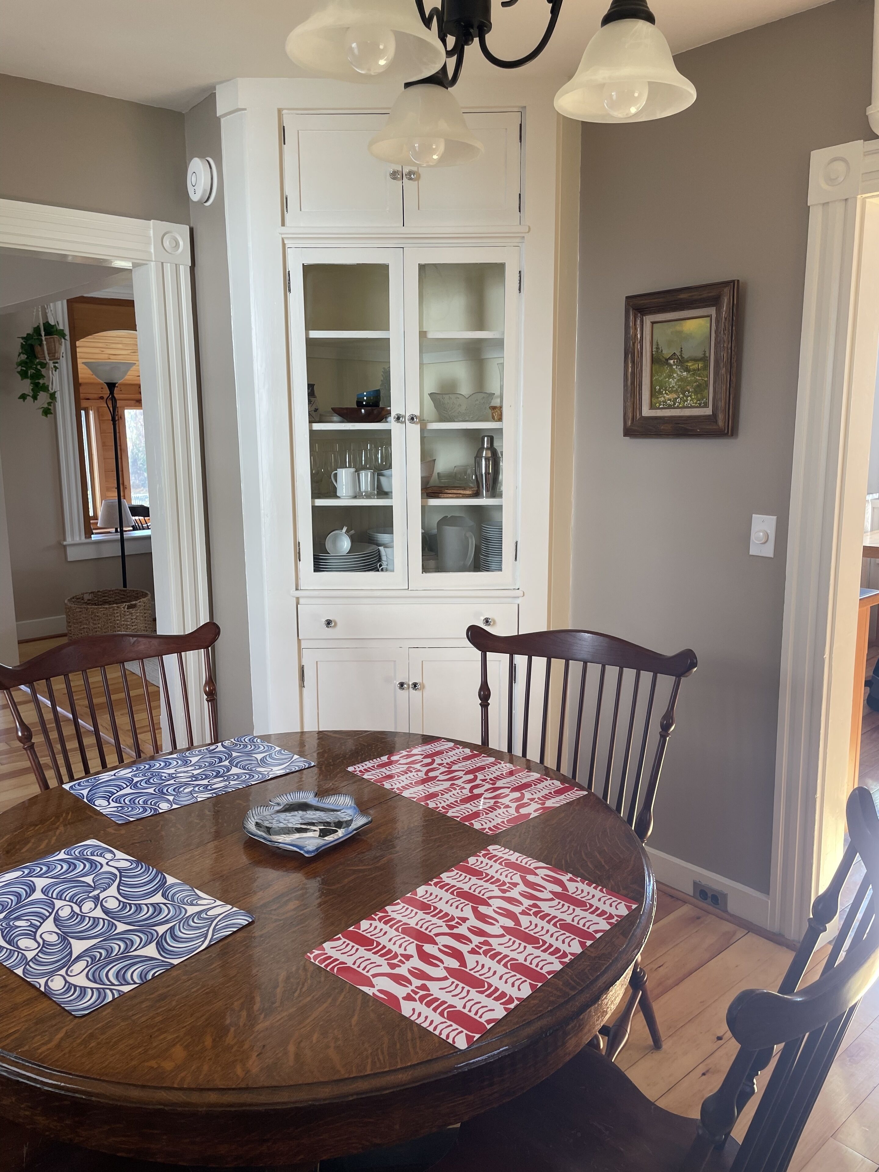 A dining area with a wooden table, four chairs, and a white cabinet with glass doors.