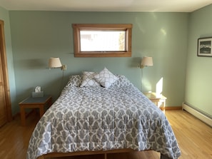 Un dormitorio con una cama, dos mesitas de noche, dos lámparas de pared, un ventanal y un cuadro en la pared.