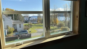 Une pièce dotée d’une grande fenêtre donnant sur un quartier résidentiel, une voiture garée et une vue sur un lac.