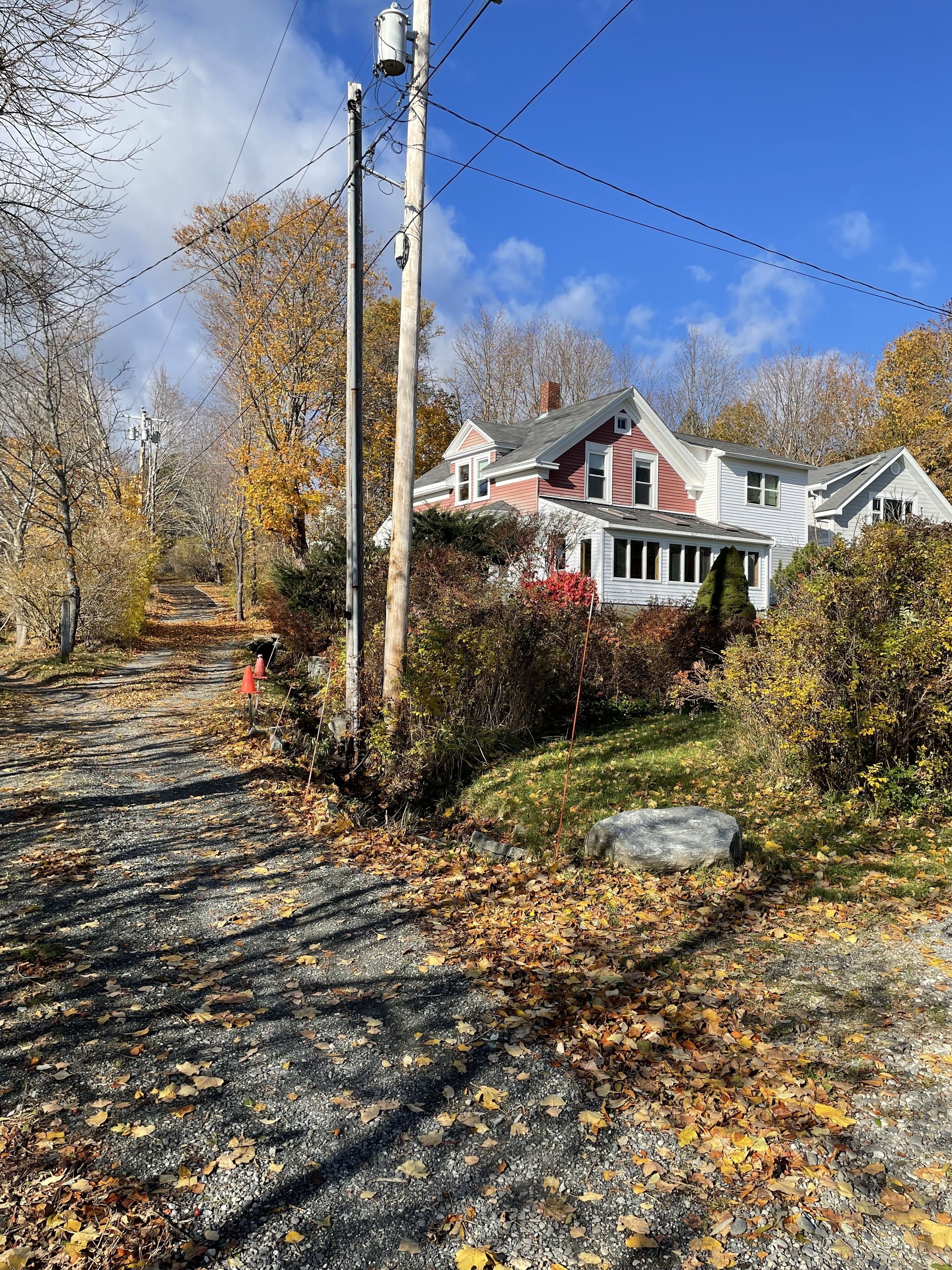 A two-story house with a red and white exterior, surrounded by trees and a gravel driveway.