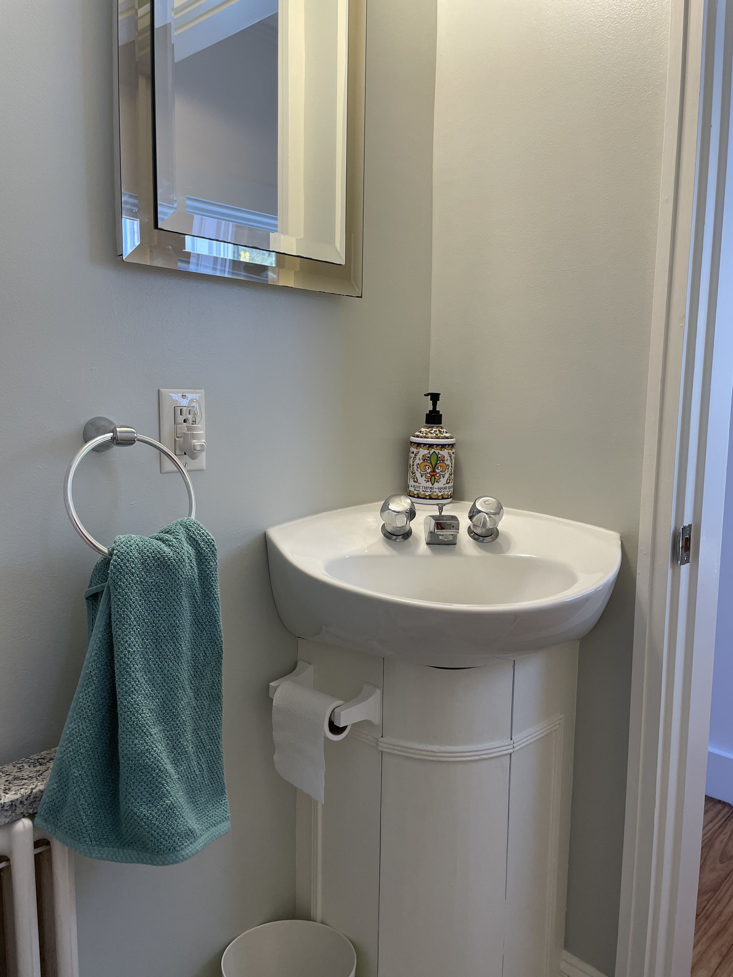 Une salle de bain avec un lavabo blanc, un porte-serviettes avec une serviette verte, un distributeur de savon et un miroir au-dessus du lavabo.