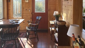 L’intérieur d’un chalet en bois comprend une table à manger, des chaises, un ventilateur de plafond, une porte rouge et une fenêtre donnant sur les arbres.