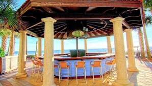 A covered outdoor bar area with a view of the ocean, featuring a central bar and multiple bar stools.