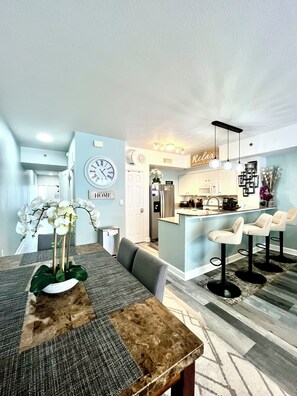 Una cocina moderna con una isla central, taburetes de bar y una zona de comedor con una mesa y sillas de madera.