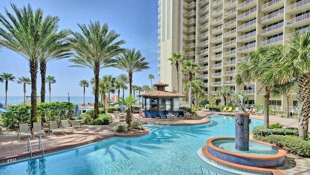 A hotel pool area with palm trees, lounge chairs, and a view of the ocean.