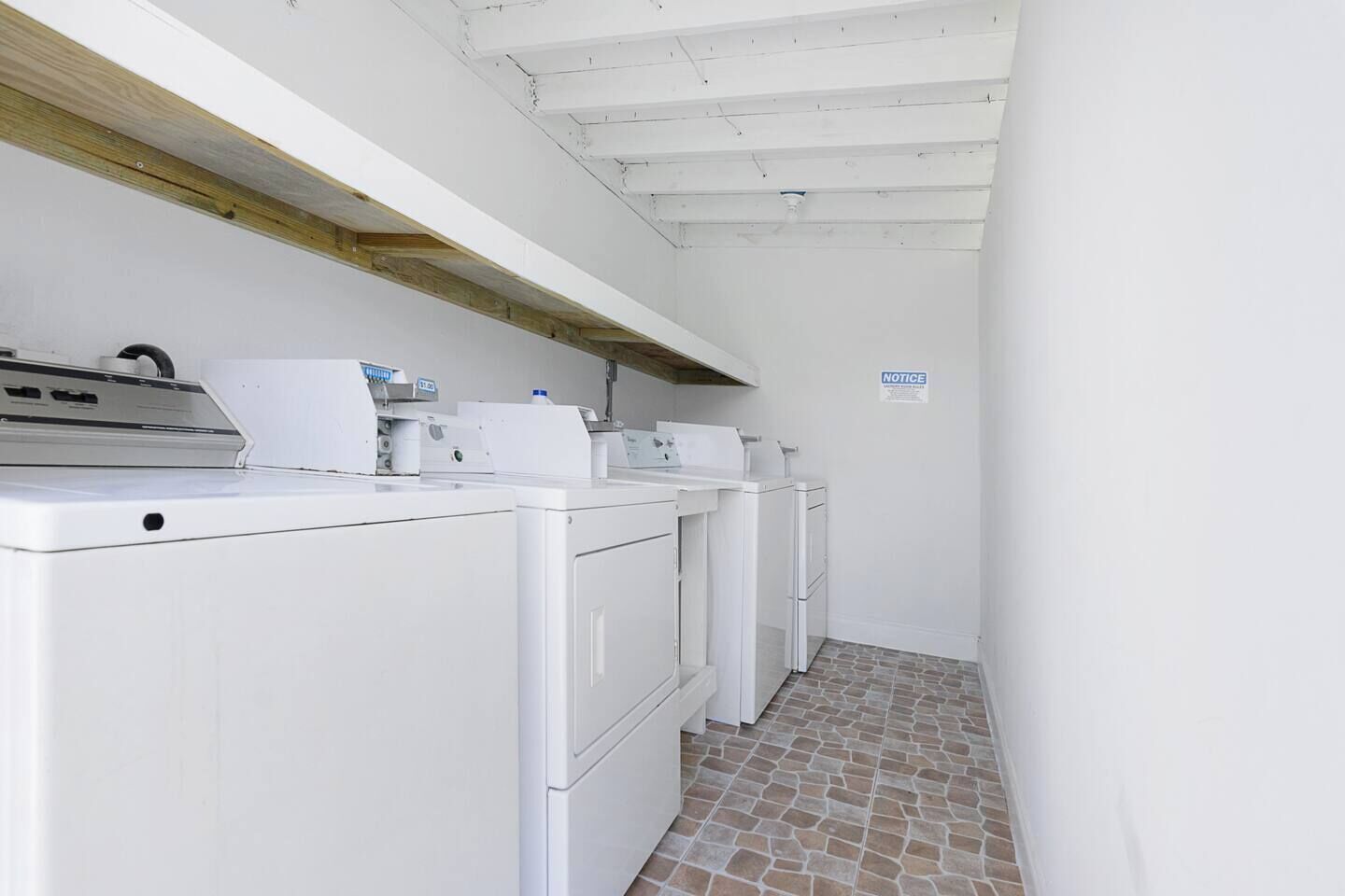 Un cuarto de lavado con electrodomésticos blancos, piso de baldosas y un letrero que dice 'NOTICE'.