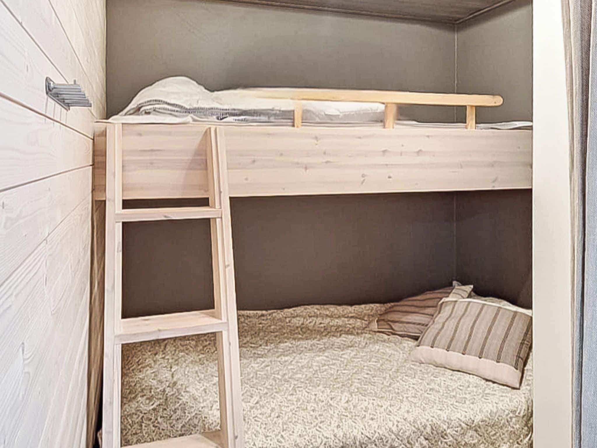 A bunk bed with a wooden ladder, a mattress, and pillows.