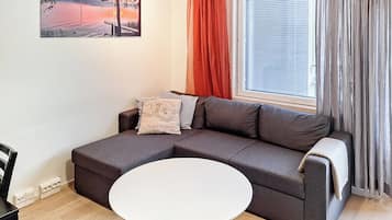 A modern living room with a sectional sofa, a round white table, and a window with curtains.