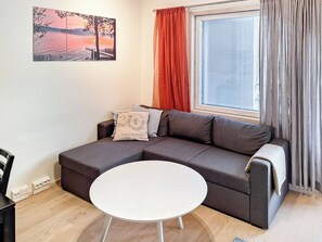Una sala moderna con un sofá modular, una mesa redonda blanca y un ventanal con cortinas.