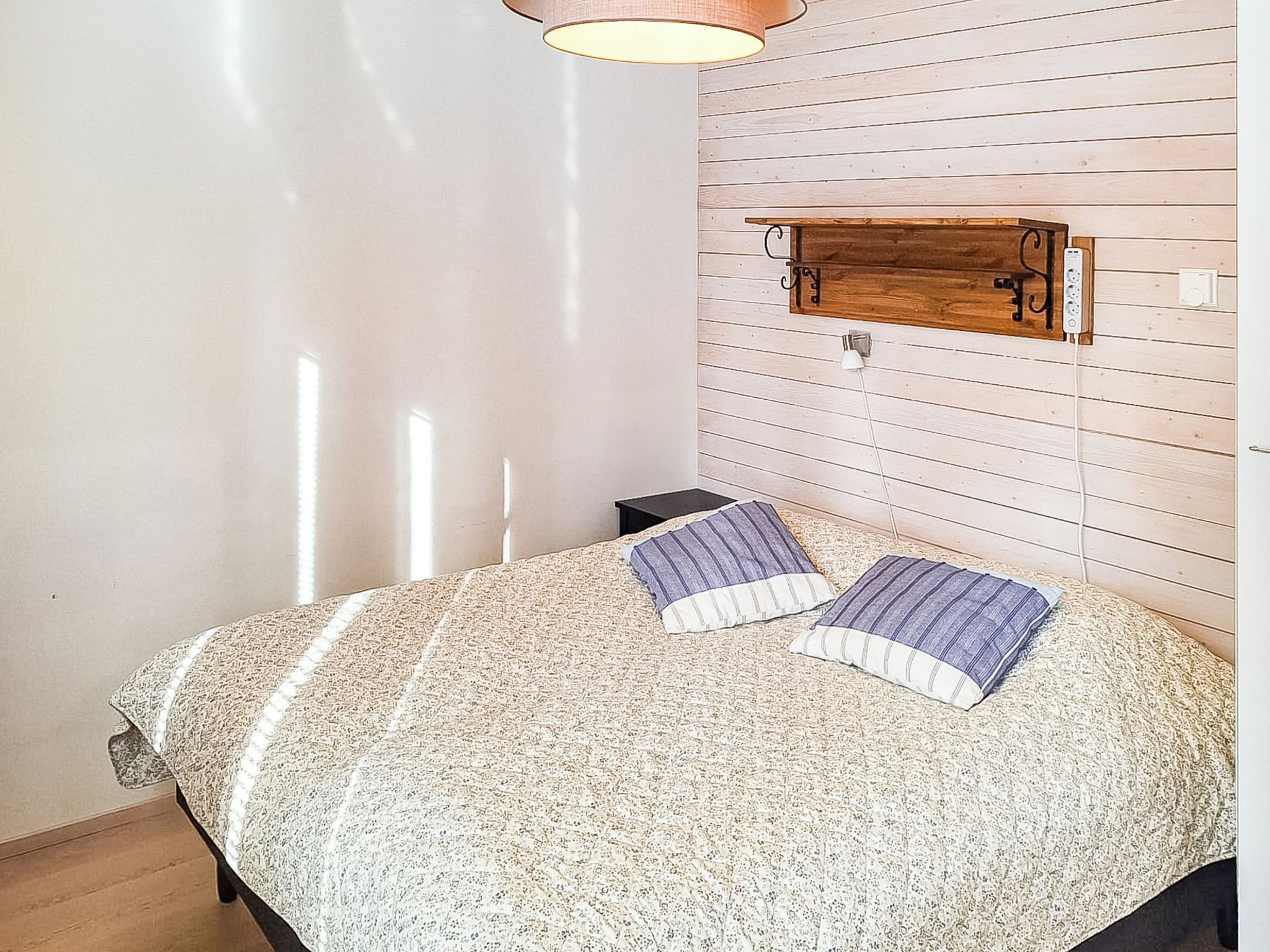 A bedroom with a bed, a nightstand, a wooden headboard, and a wall-mounted light fixture.