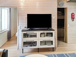 A modern living room with a flat-screen TV on a white cabinet, a window with curtains, and a visible door leading to another room.