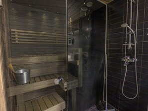 A sauna with a wooden bench, a metal bucket, and a glass door.