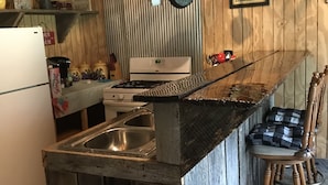 Una cocina rústica con paredes de madera, una isla integrada con un fregadero, estufa y ollas colgantes.