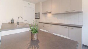 A modern kitchen with white cabinets, a stainless steel sink, and a central island with a potted plant. - Medano 1.2 with balcony by Interhome (Bredene)