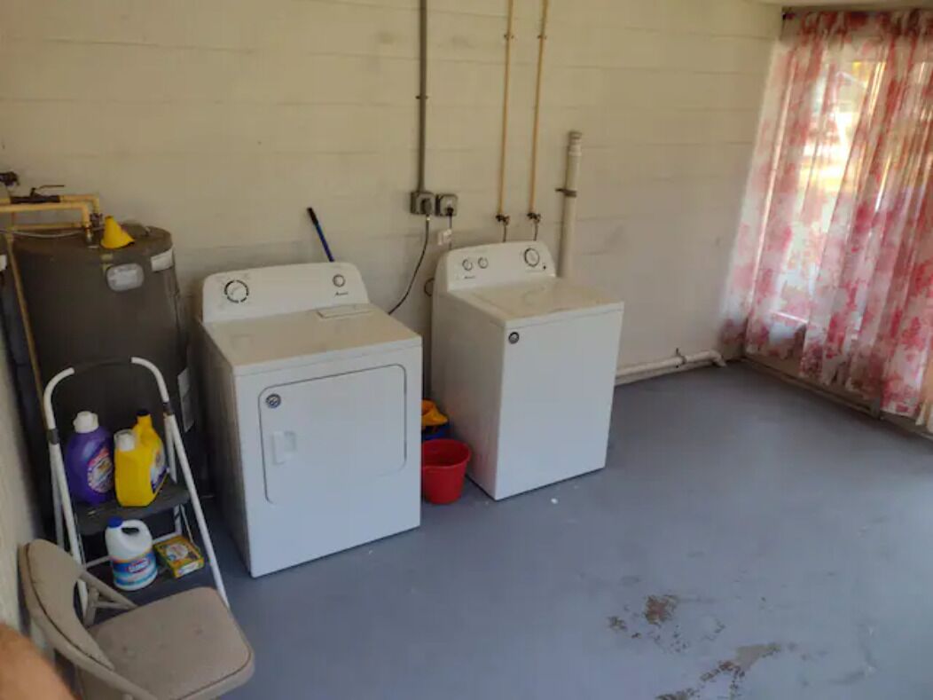 A laundry room with two washing machines, a folding table with cleaning supplies, and a chair.