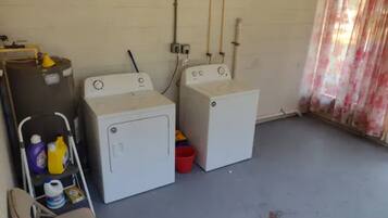 A laundry room with two washing machines, a folding table with cleaning supplies, and a chair.