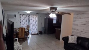 Ein Wohnzimmer mit einer schwarzen Ledersofa, einem weißen Sessel und einem Essbereich inklusive Tisch und Stühlen.