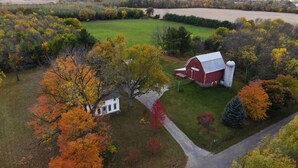 Une vue aérienne d’une ferme avec une grange rouge, une tour à grain et une maison blanche, le tout entouré d’arbres aux couleurs automnales.