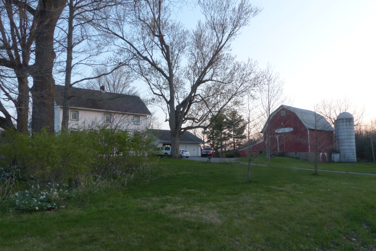A rural setting with a house, a barn, and a silo.