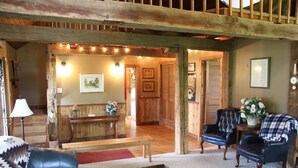 Un intérieur rustique avec un banc en bois, des fauteuils en cuir, une petite table et un escalier menant à une autre pièce.