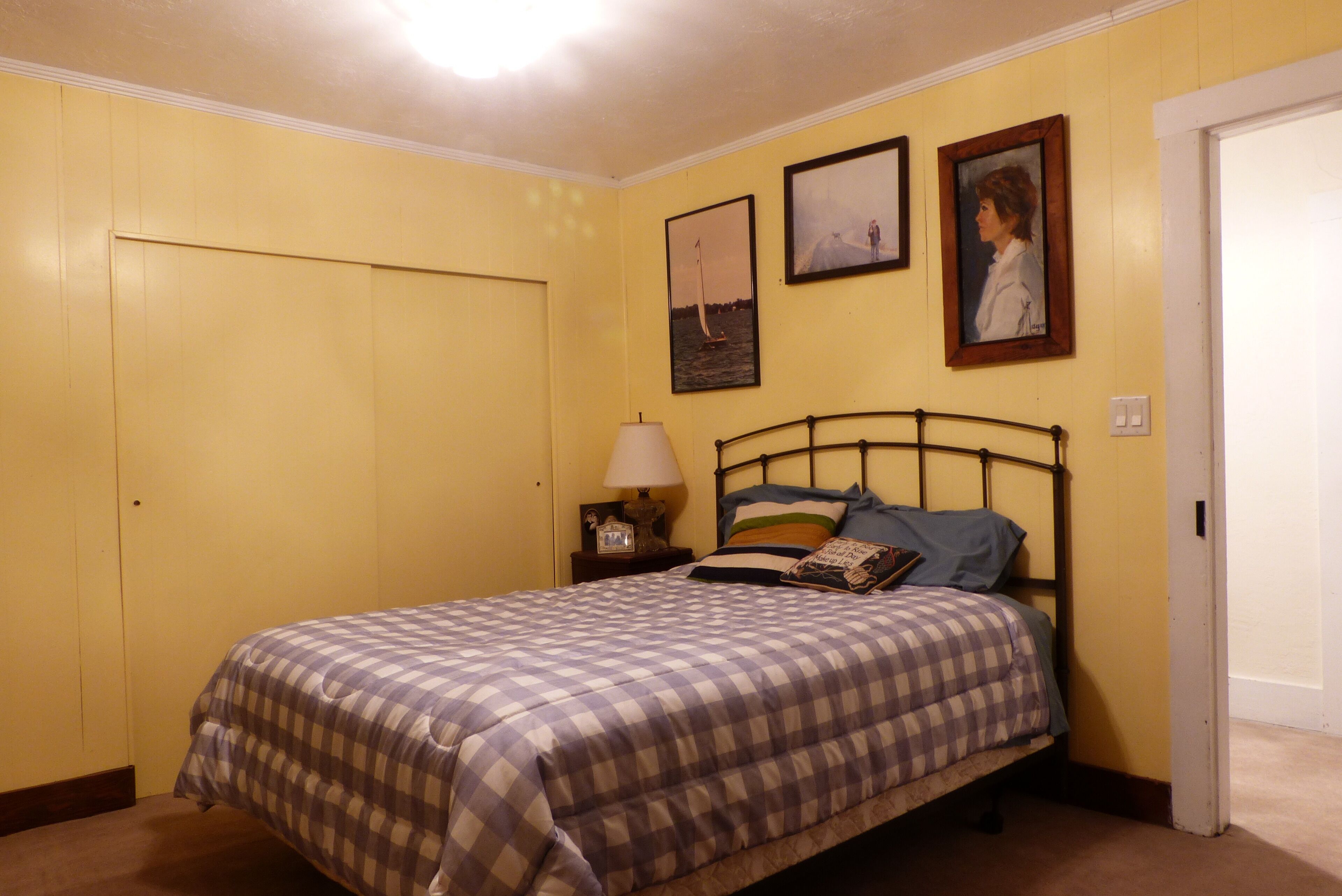 A bedroom with a bed, a nightstand, a lamp, and two framed pictures on the wall.