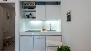 Une cuisine compacte équipée d’un lave-vaisselle, d’un évier et d’un petit plan de travail. On aperçoit une chaise et une table au premier plan, et une plante en pot sur la table.