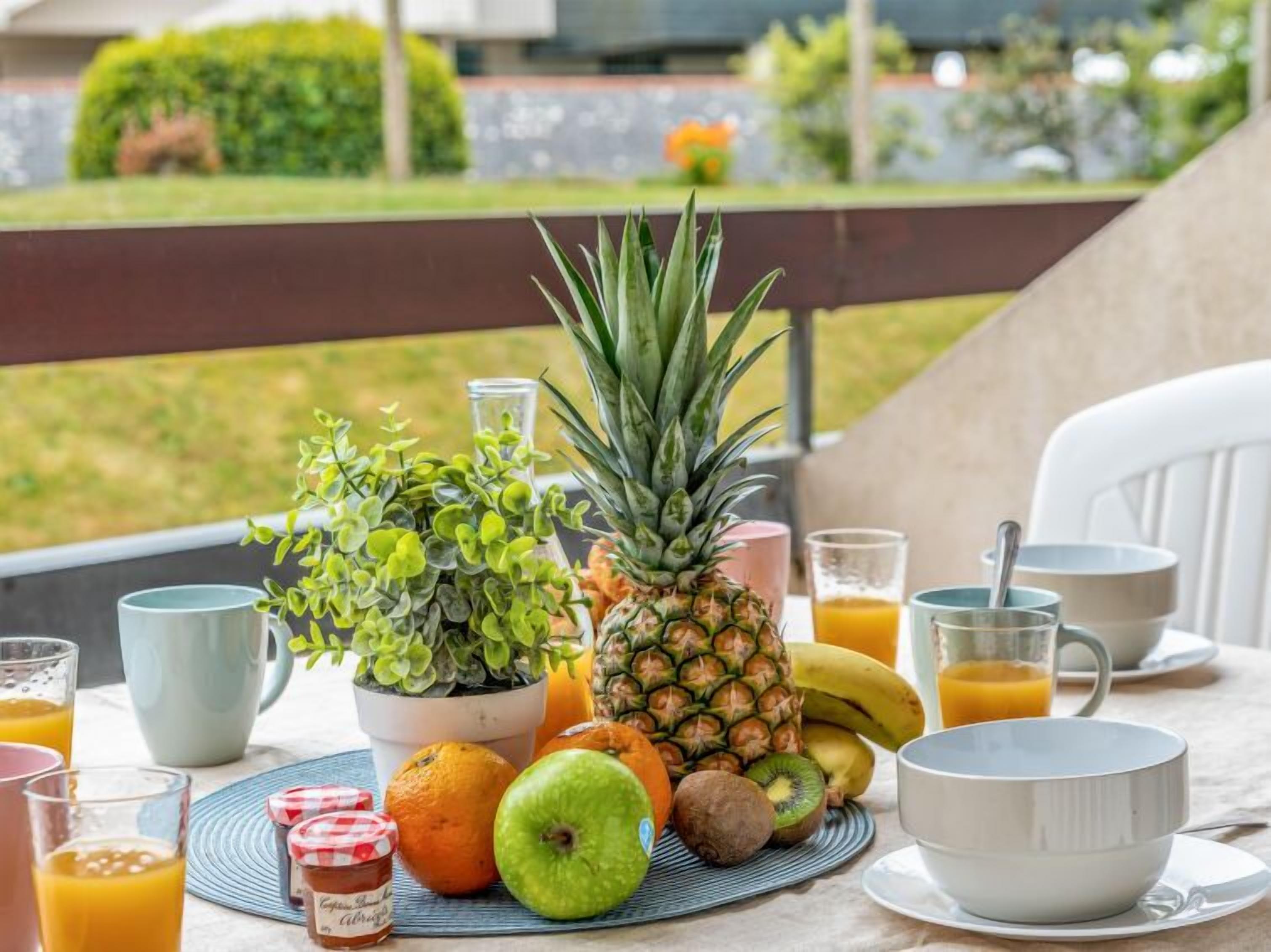 Ein Frühstückstisch mit Früchten, einer Pflanze und Getränken auf einer Terrasse.