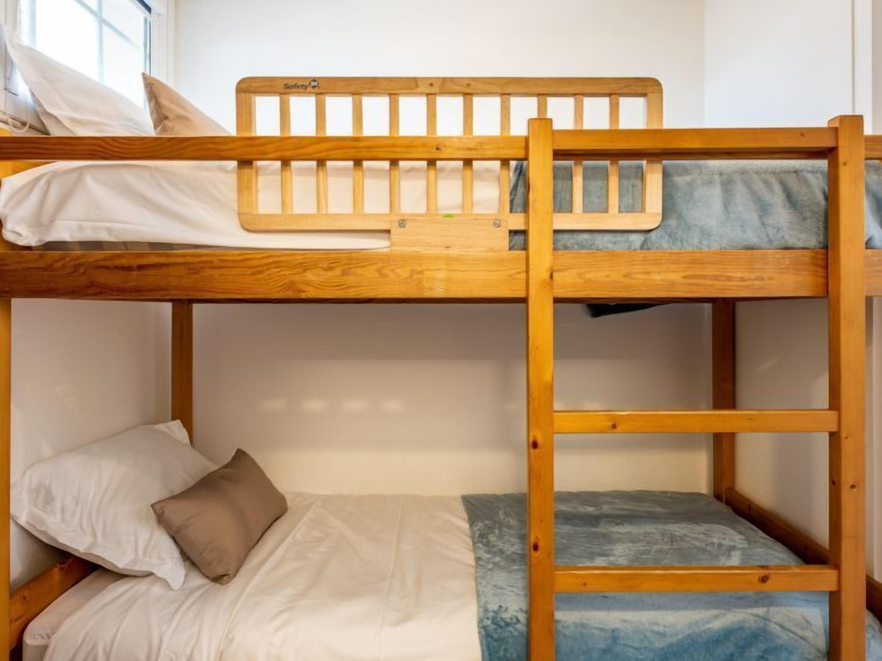 A bunk bed with a wooden frame, white bedding, and a blue mattress cover.
