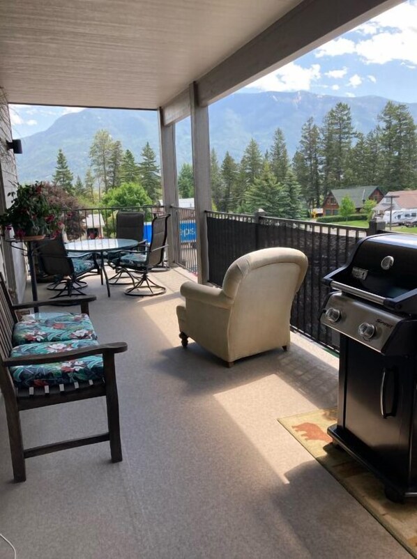 Enjoy a meal with a mountain view from this balcony, featuring a dining table for two, two chairs, and a comfortable armchair.