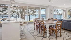 Een moderne keuken met een centraal eiland, een eethoek met stoelen, een bank en grote ramen met uitzicht op zee.