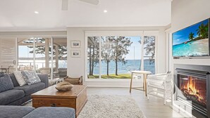 Een moderne woonkamer met een open haard, een bank, een salontafel en uitzicht op zee door grote ramen.