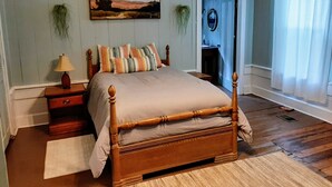 Una camera da letto con un letto in legno, un comodino, una lampada, un quadro e una porta che dà su un bagno.