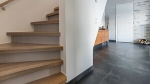 Ein modernes Interieur mit einer Holztreppe, einer weißen Wand und einem schwarzen Fliesenboden.