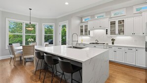 Una cocina moderna con muebles blancos, una isla grande con taburetes de bar y una lámpara colgante.