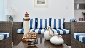 A room with a striped sofa, a small table with a ship model and a lighthouse, and a framed picture on the wall.