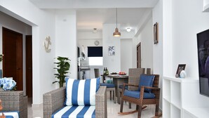 A modern living room with wicker furniture, a dining area, and a kitchen in the background.