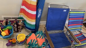Una habitación con una silla de playa azul, una toalla de playa a rayas y un bolso colorido.