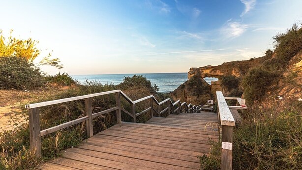 Un escalier en bois mène à une plage d’où l’on a une vue dégagée sur l’océan et les falaises rocheuses.