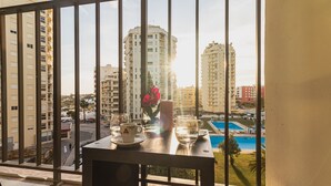 Un balcon avec une table dressée pour deux personnes, donnant sur une piscine et des immeubles de grande hauteur.