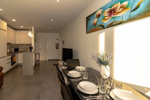 Une cuisine moderne avec des meubles blancs, un îlot central et un coin repas avec une table dressée pour quatre personnes.