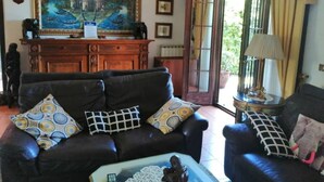A living room with a black leather sofa, patterned cushions, a coffee table, a painting, a cabinet, and a lamp. - 3 bedrooms villa  Sleeps 6 with Garden (Roma)
