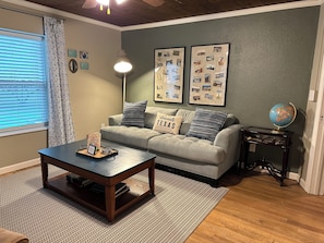 A living room with a sofa, a coffee table, a globe, and framed photos on the wall.